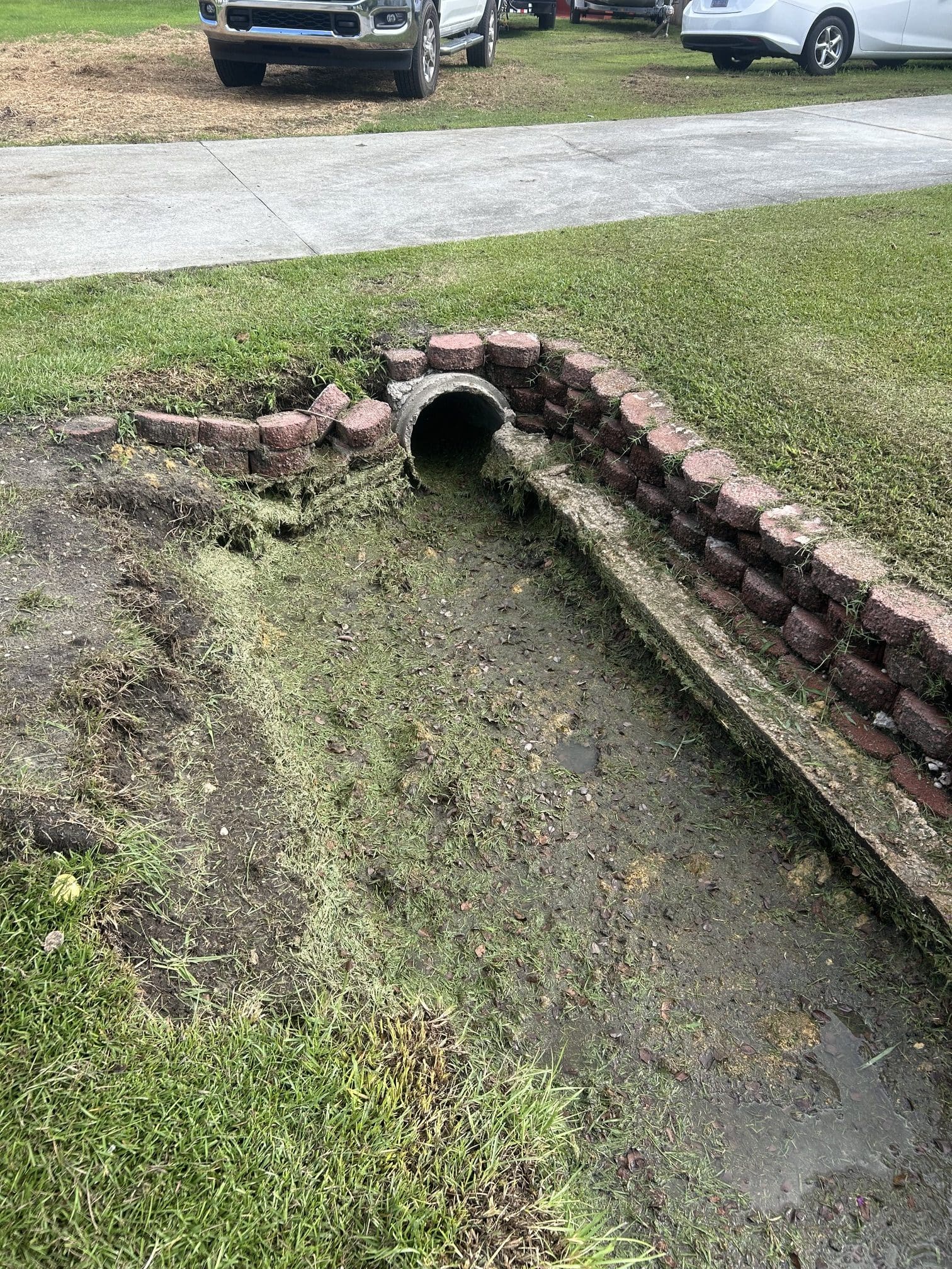 Grassed roadside ditch line in a residential neighborhood before cleaning